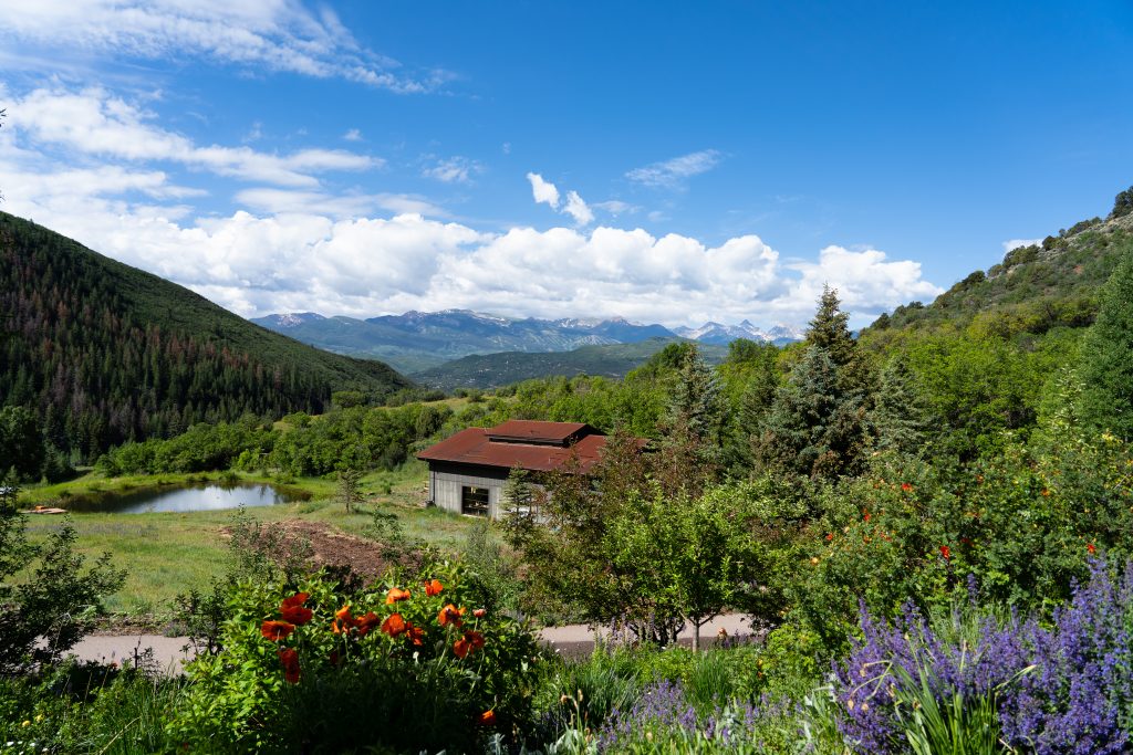 beautiful view with garden in foreground, building in middle ground next to a pone, with the Elk Mountain range in the background.